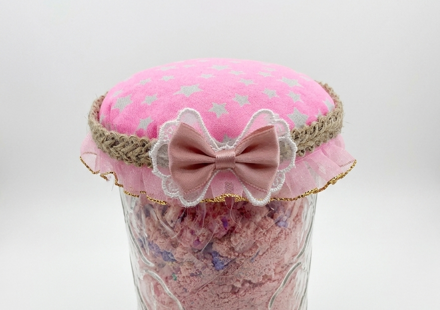 Jar of pink bath salts with a decorative headband and bow on a white background