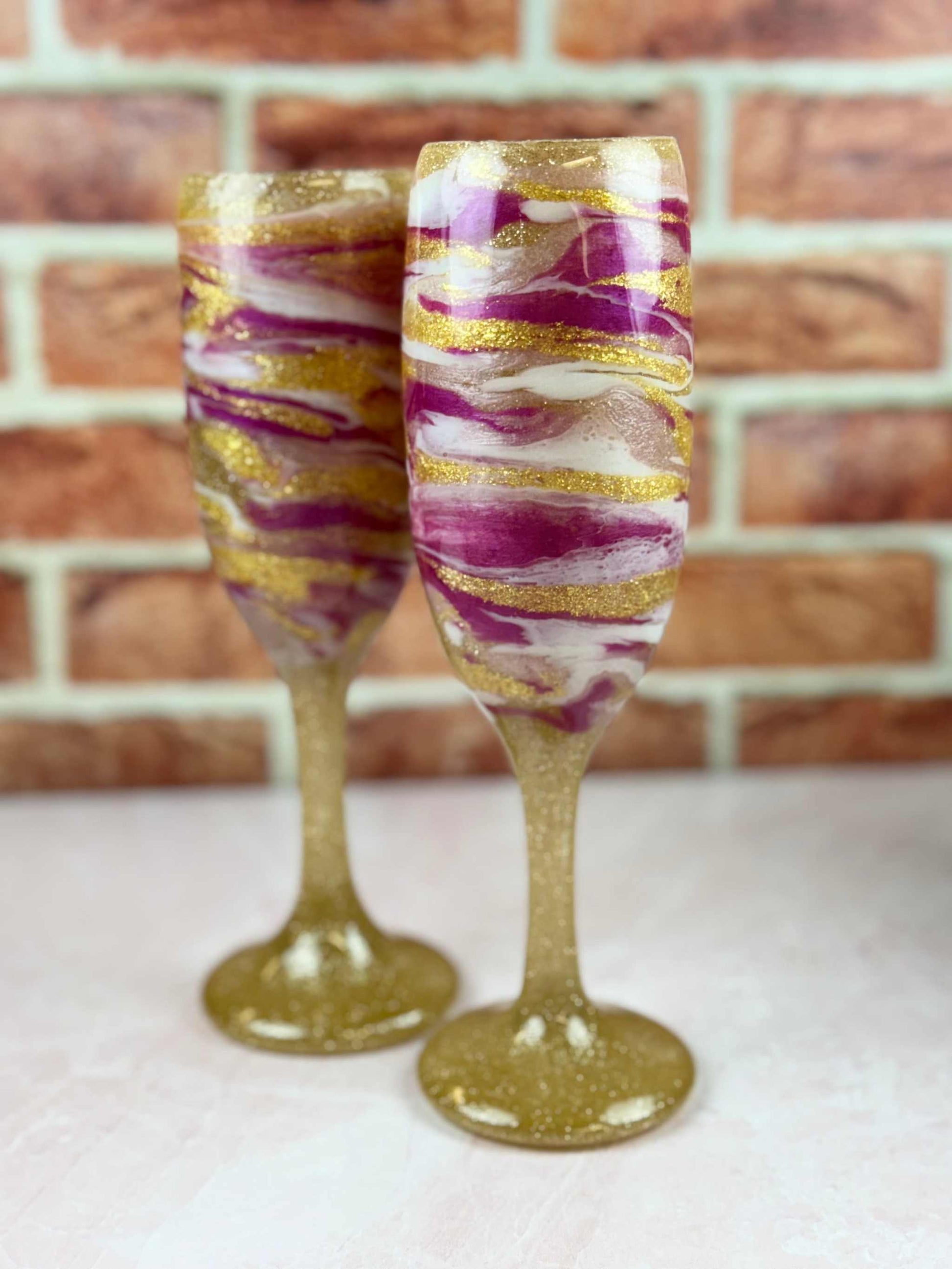 Set of 2 elegant champagne flutes with gold, pink, and white swirl design on sturdy bases