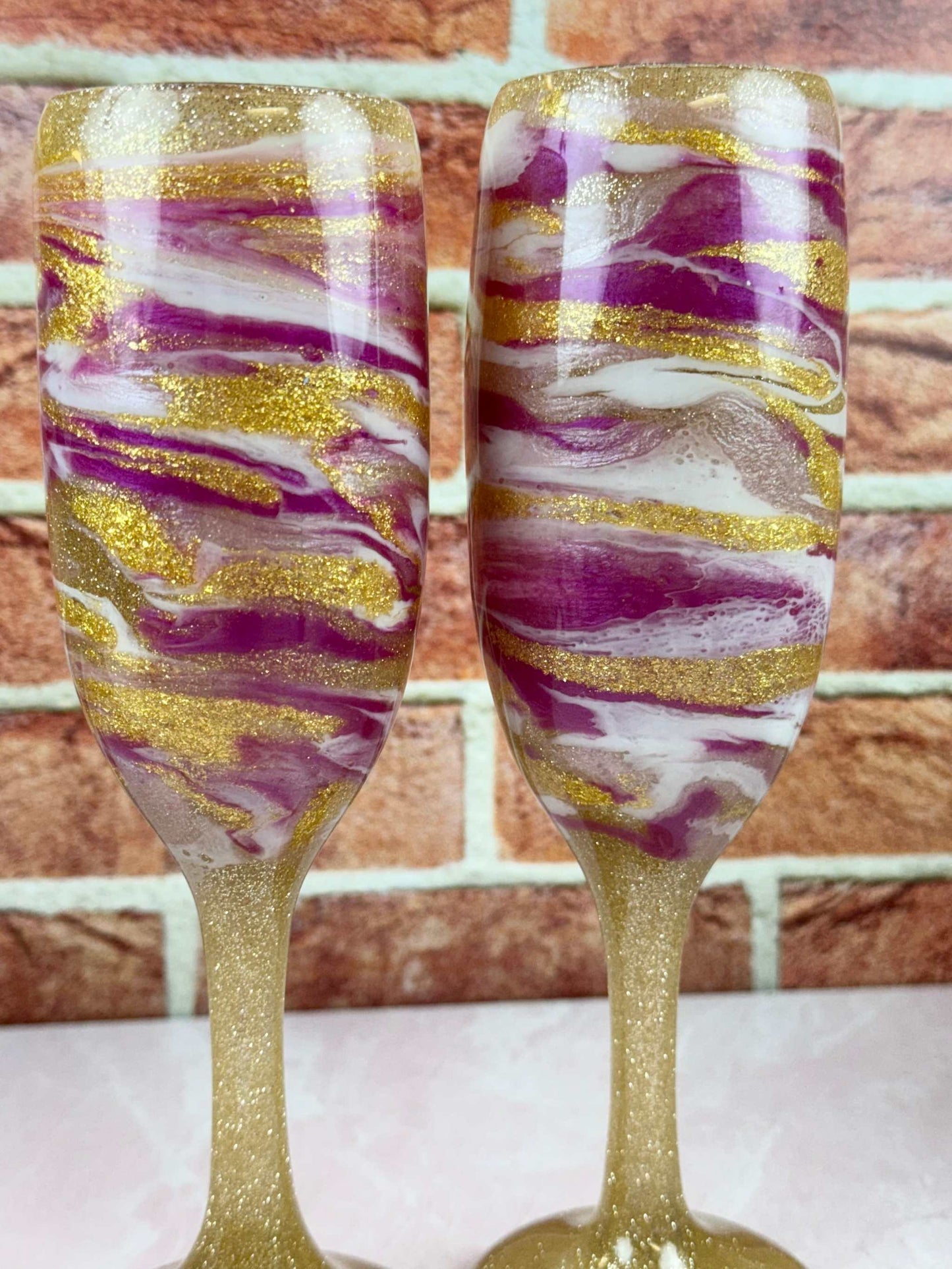 Set of 2 elegant champagne flutes with gold, pink, and white swirl design on sturdy bases