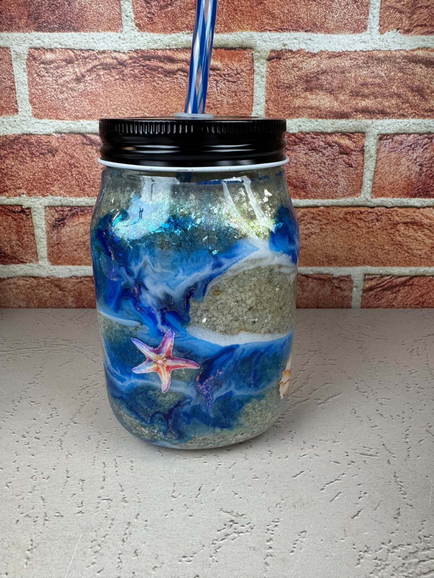 Seashell Mason Jar Mug with blue ocean design, sand texture, starfish detail, black lid, and blue striped straw 