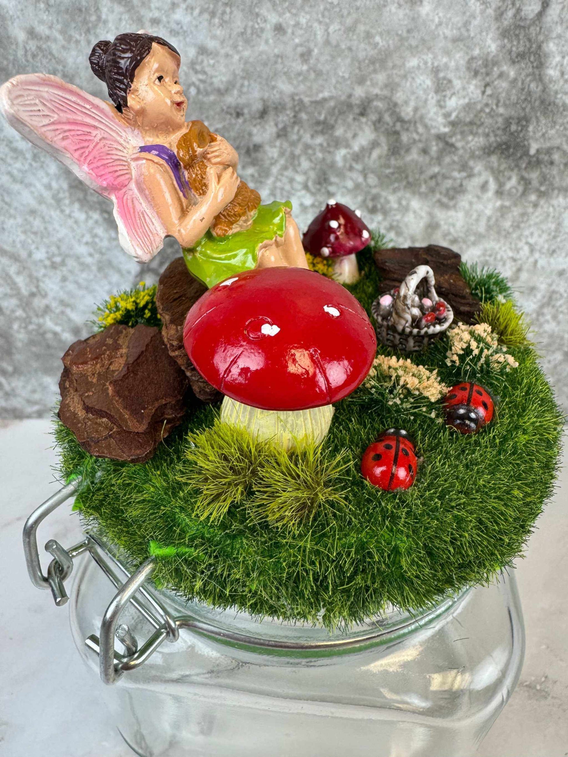 Magical fairy garden themed jar with fairy figurine, red mushroom, and ladybugs on grass lid decor