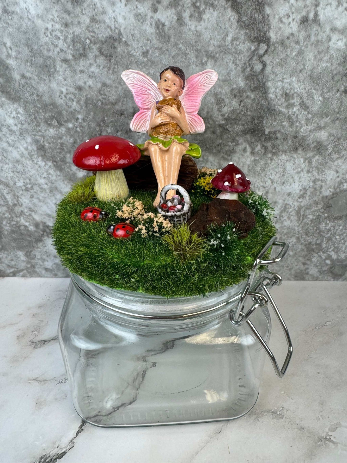 Magical fairy garden themed glass jar with fairy figurine, mushrooms, and greenery decoration