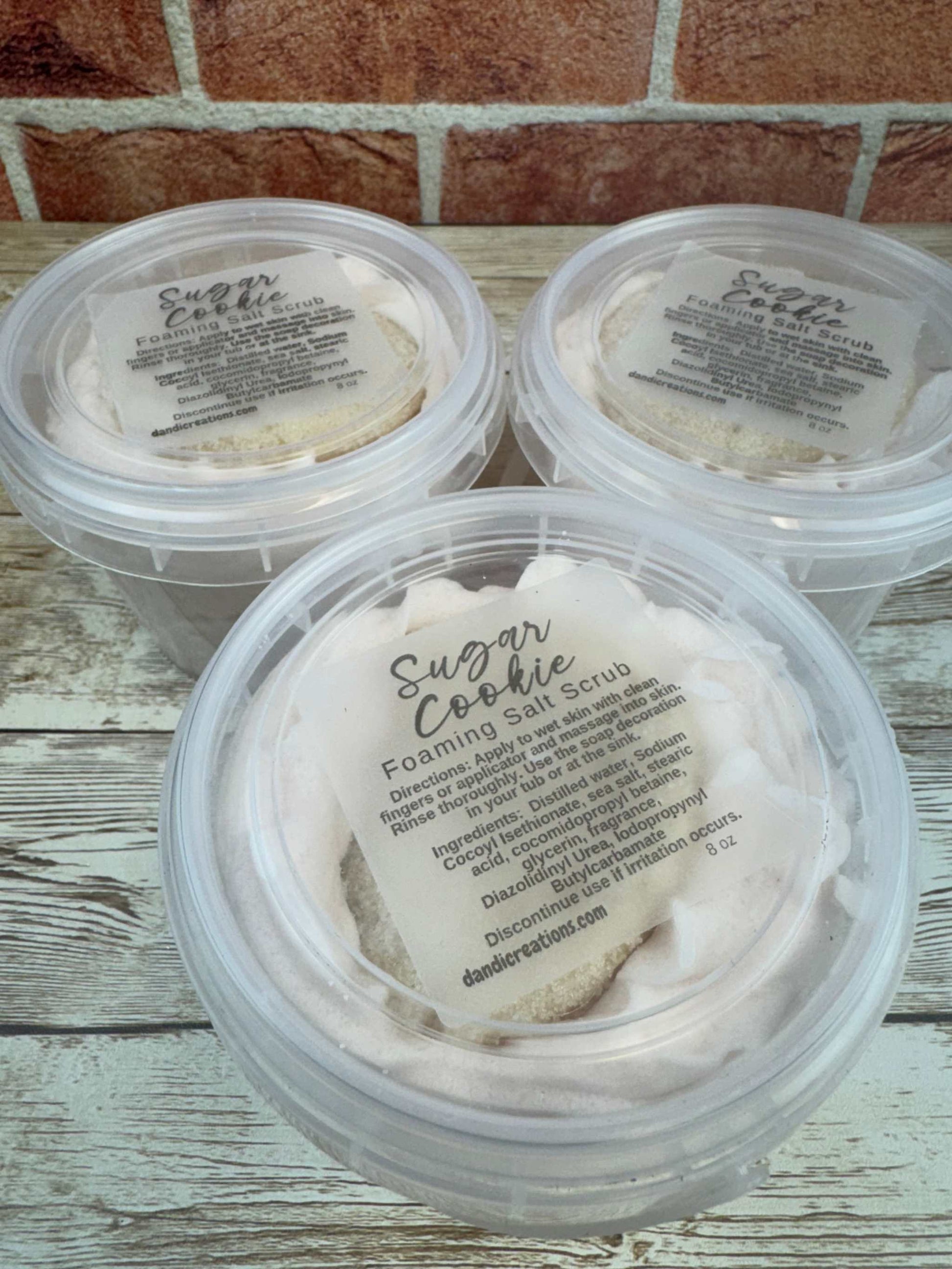 Foaming Salt Scrub Sugar Cookie whipped soap exfoliating sea salt skincare product in clear round containers on wooden surface