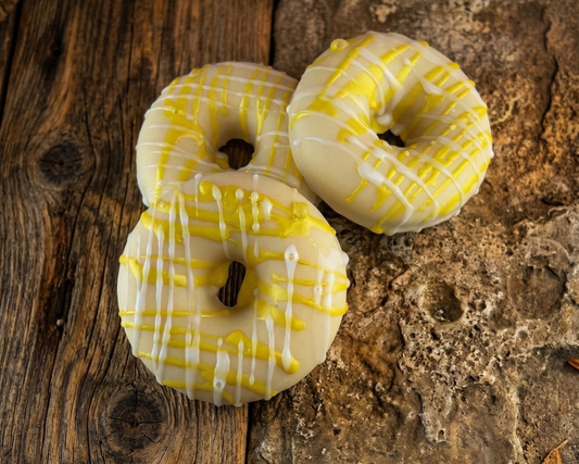 Three donuts with yellow and white glaze on a rustic wooden surface