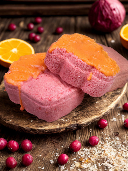 Pink and orange bath bombs on a wooden surface with cranberries and oranges.