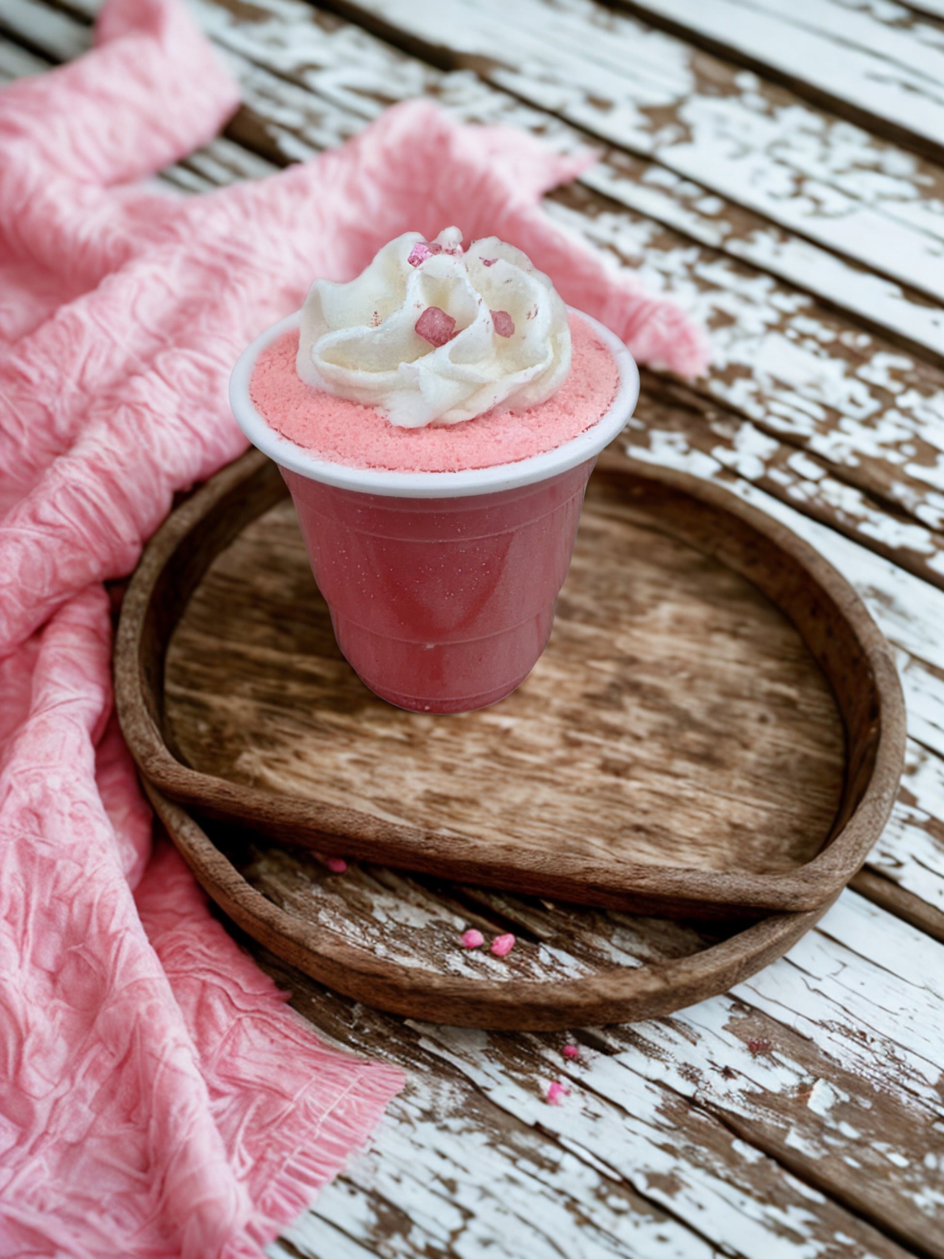 Pink cup with whipped cream and sprinkles on a wooden surface with pink fabric